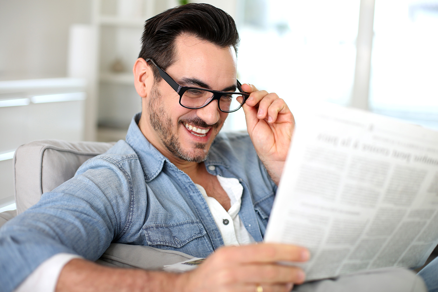 Hymyilevä mies lukee sanomalehtiä pitäen silmälaseistaan toisella kädellä kiinni.