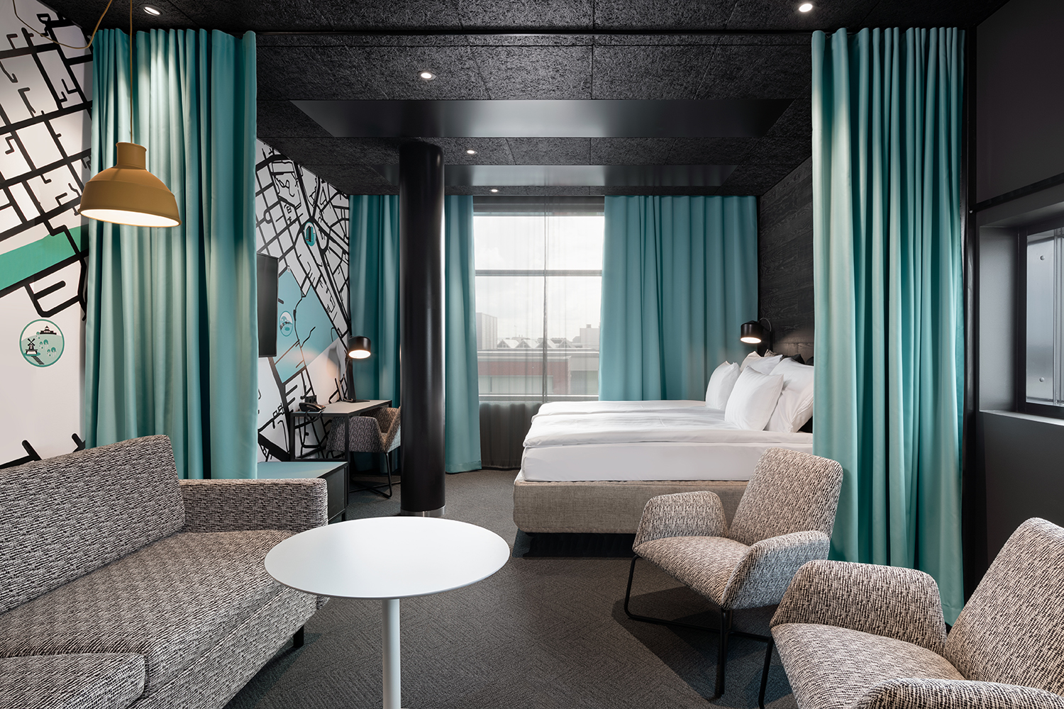 Sokos Hotel Kupittaan hotellihuone, jossa on turkoosit verhot, harmaa sohva ja kaksi nojatuolia sekä sänky. Seinillä on sisustustapetit.